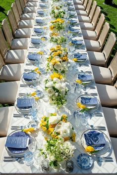 a long table is set with blue and white plates, yellow flowers, and glassware