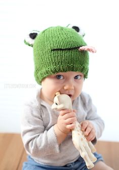 a baby wearing a green knitted hat eating a bone