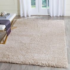 a white rug on top of a wooden floor next to a window with curtains behind it