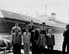 a group of men standing next to each other in front of a boat