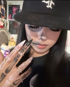 a woman with fake nails and makeup is holding her hand up to the camera while wearing a baseball cap