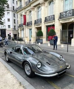 a silver sports car parked on the street in front of a building with people walking by