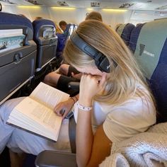 a woman sitting in an airplane reading a book and wearing headphones on her ears