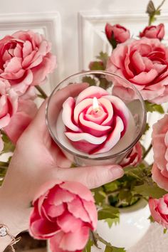 a person holding a small glass bowl filled with pink flowers on top of a table