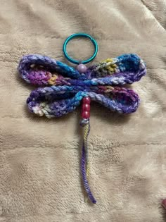 a crocheted dragonfly is laying on a bed with a blue ring around it's neck