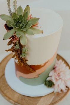 a white and pink cake with succulents on top sitting on a wooden plate