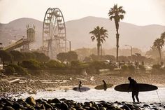 two surfers are standing in the water with their surfboards near an amusement park