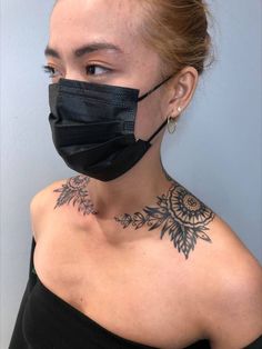 a woman wearing a black face mask with tattoos on her chest and neck, looking at the camera