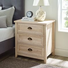 a nightstand with two drawers and a lamp on top of it next to a bed