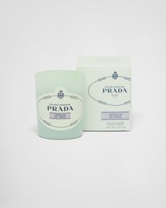 a green candle sitting next to a box on a white surface with the words prada written in it