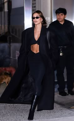 the model is seen walking down the street in her black outfit and matching coat, which she