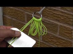 a hand holding a piece of white paper next to a green string hanging from a hook on a brick wall