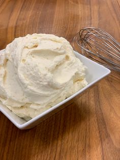 a white bowl filled with whipped cream next to a whisk on top of a wooden table