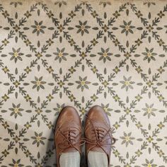 a pair of brown shoes sitting on top of a floor next to a floral wallpaper