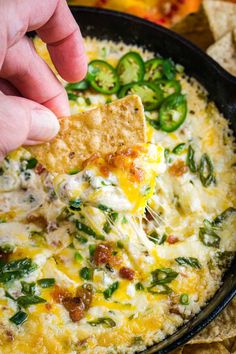 a hand dipping a tortilla chip into a skillet filled with cheese and vegetables