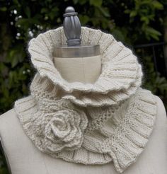 a white knitted scarf with a flower on the front and side, sitting on top of a mannequin