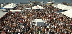 a large group of people standing in front of white tents at an outdoor event near the water