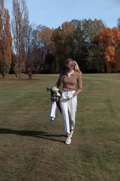 a woman walking across a grass covered field holding a golf club in her right hand