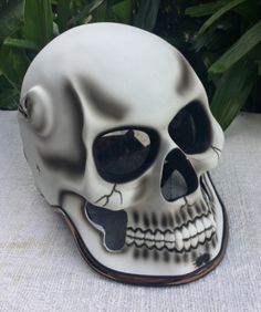 a white and black skull mask sitting on top of a table next to green plants