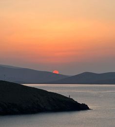 the sun is setting over water with hills in the background