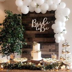 a table topped with lots of white balloons next to a cake and cupcakes