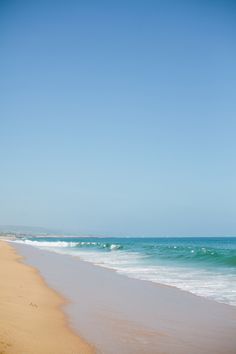 two people walking along the beach with surfboards