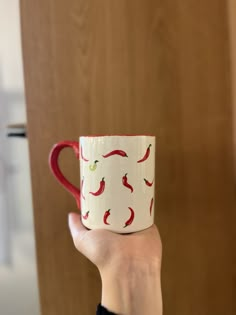 a hand holding a red and white coffee cup with chili peppers on the inside, in front of a wood paneled wall