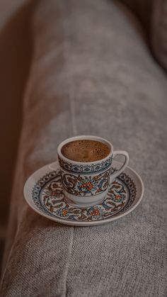 a cup of coffee sitting on top of a saucer next to a sofa cushion