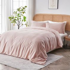 a bed with pink sheets and pillows in a room next to a plant on the floor