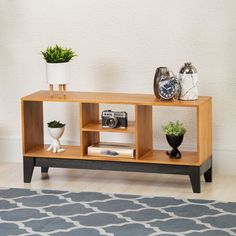 a wooden shelf with two plants and an alarm clock on it next to a rug