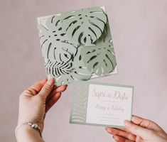 a person holding up a card that says save the date and palm leaves on it