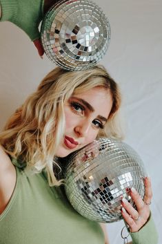 a woman holding two disco balls in front of her face and looking at the camera