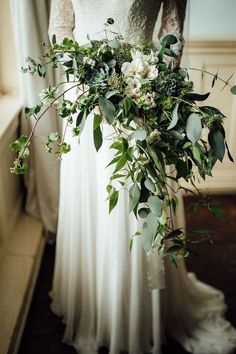 a bride holding a bouquet of greenery and white flowers in her wedding day dress