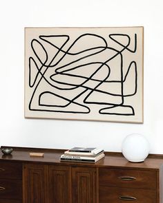 an abstract painting hangs on the wall above a dresser