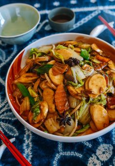 a bowl filled with stir fried vegetables next to chopsticks and a cup of tea