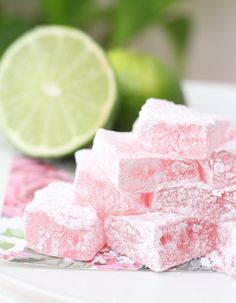 a pile of pink and white marshmallows next to a lime on a plate