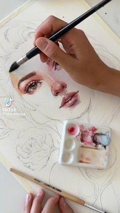 a person is drawing on a piece of paper with a brush and watercolor pencils