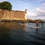 a group of people on surfboards in the water near a stone wall and lighthouse