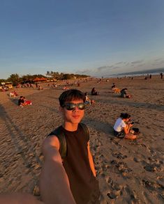 a man taking a selfie on the beach with people laying in the sand behind him