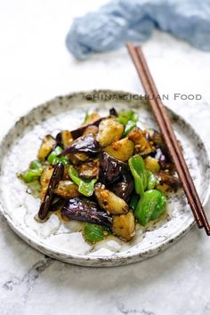 a white plate topped with stir fried vegetables and chopsticks next to a blue towel