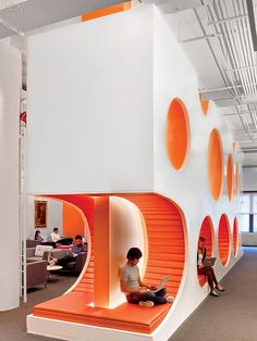 an orange and white room with people working on laptops in the area that looks like a spiral staircase