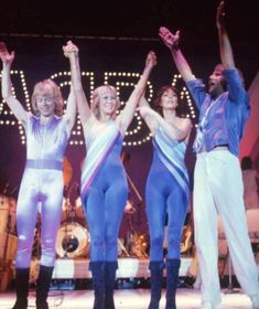 four people in blue and white outfits on stage with their hands up to the sky