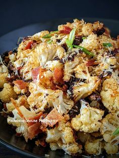 a black plate topped with cauliflower covered in cheese and seasoning sprinkles