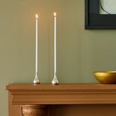 three candles sitting on top of a mantle next to a bowl