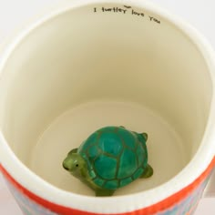 a ceramic turtle sitting in a cup with writing on the bottom and inside it's lid