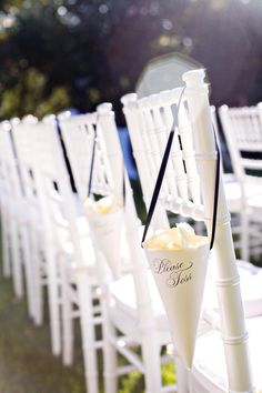 white chairs are lined up with flower vases on the back of them for an outdoor ceremony