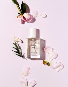 a bottle of perfume next to flowers on a pink background