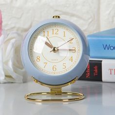 a blue alarm clock sitting on top of a table next to books and a vase