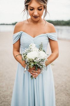 a woman in a blue dress holding a bouquet and looking down at the ground with her hands on her hips