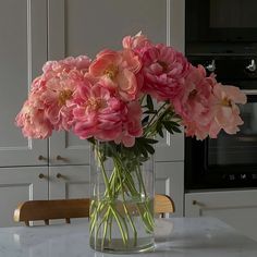 a glass vase filled with pink flowers on top of a kitchen counter next to an oven